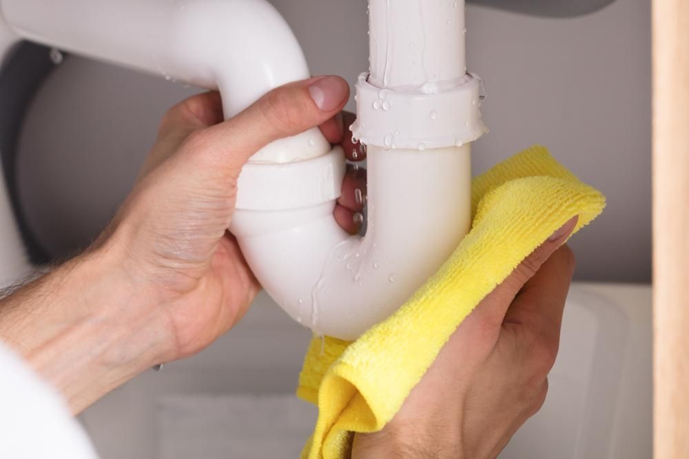 Hands Wiping a Wet, White Sink Pipe With a Yellow Cloth — ABV Plumbing In Woy Woy, NSW