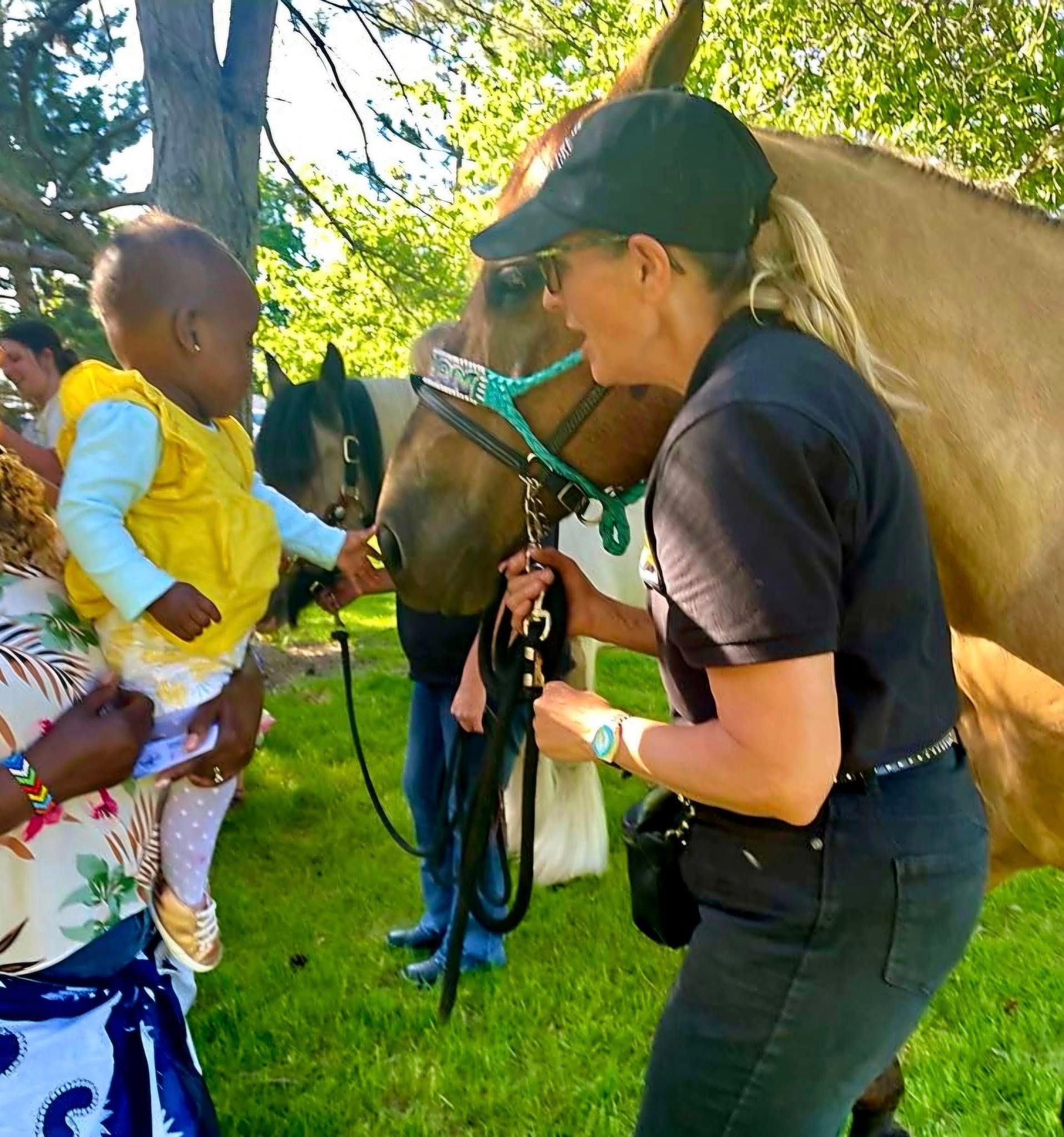 A woman holding a baby petting a horse