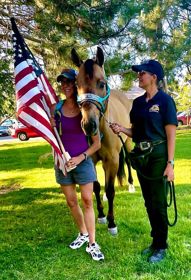 Two women are standing next to a horse holding an american flag.