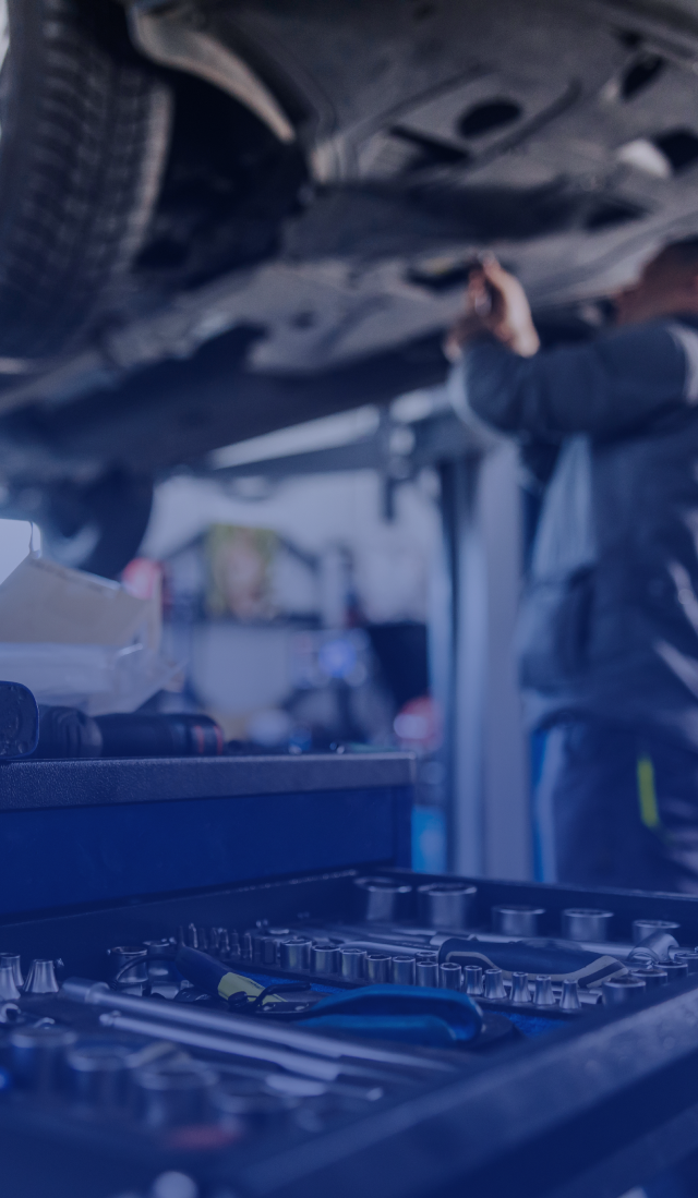 Mechanic working under a car with tools on a workbench in the foreground | Speedway Auto Care