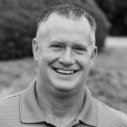 A man in a striped shirt is smiling in a black and white photo.