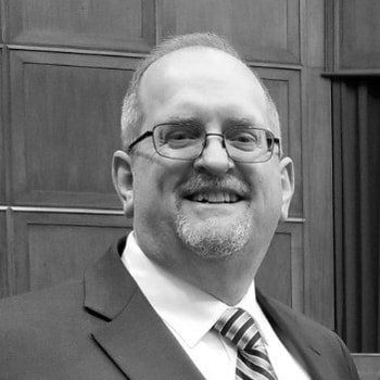 A man in a suit and tie is smiling in a black and white photo.