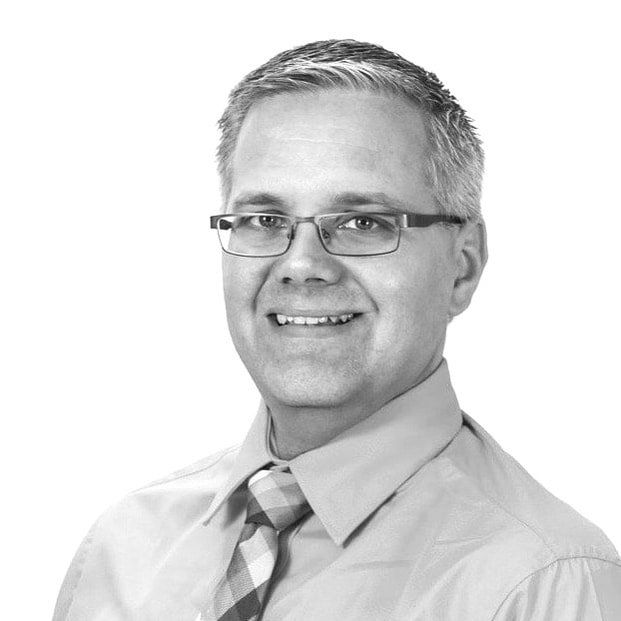 A man wearing glasses and a tie is smiling in a black and white photo.