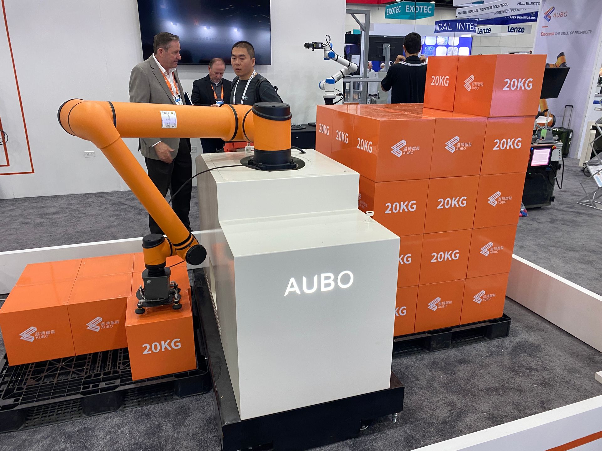 A robotic arm is standing next to a stack of orange boxes.