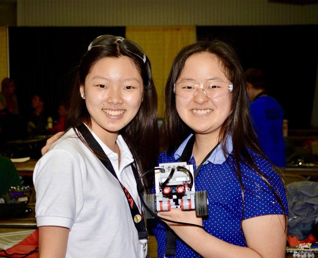 Two girls are standing next to each other holding a robot.