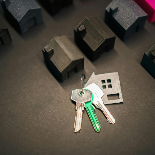Real estate deal: Small wooden house on contract, keys, calculator, and hands of two people at a table.