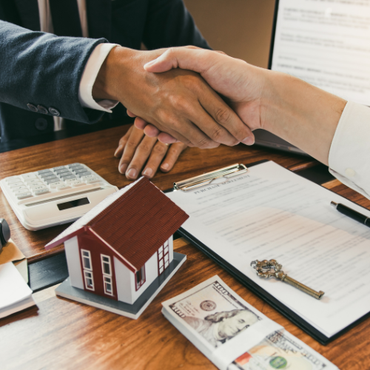 Real estate agent showing client a house model and paperwork at a desk.