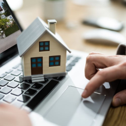 Real estate agent showing client a house model and paperwork at a desk.