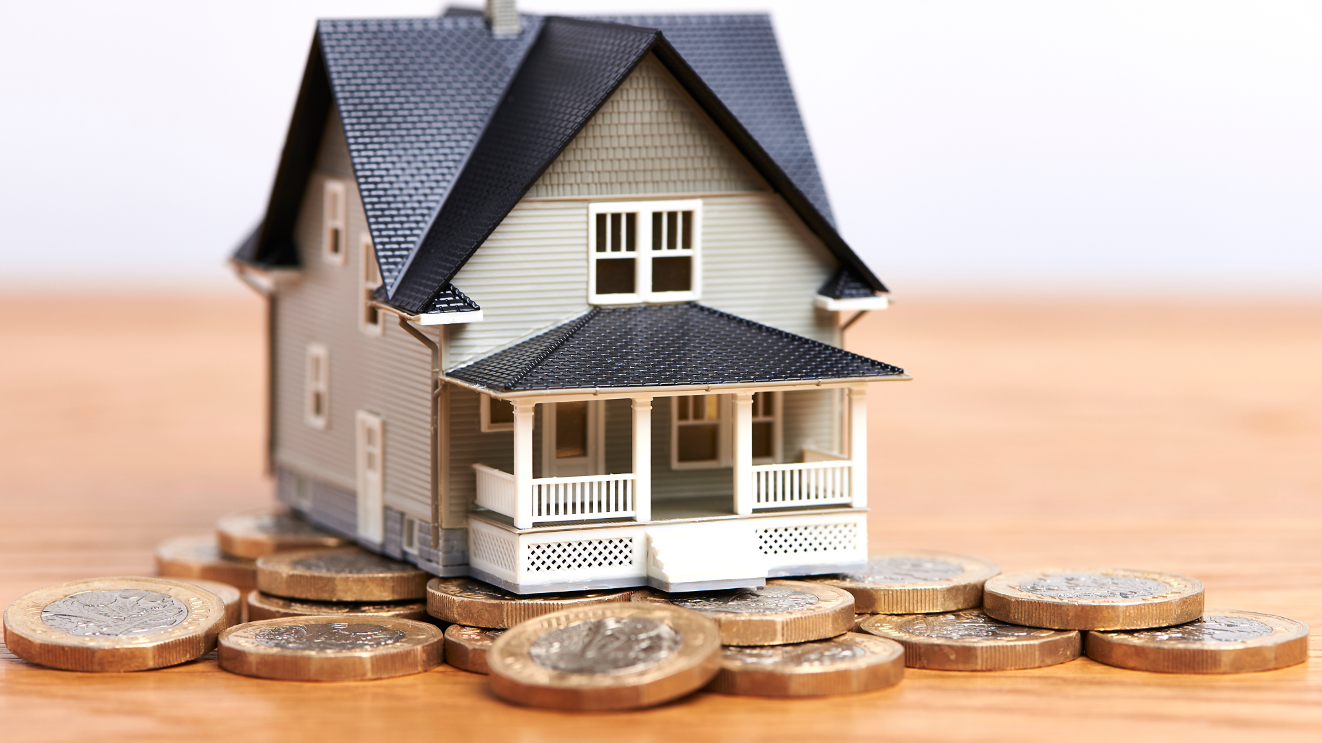 Toy house sits atop a pile of coins, symbolizing home ownership and finances.