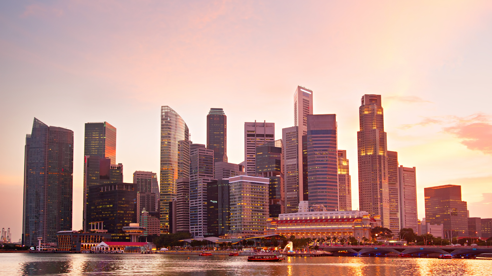 Skyline of Singapore at sunset; skyscrapers reflect golden light on the water.