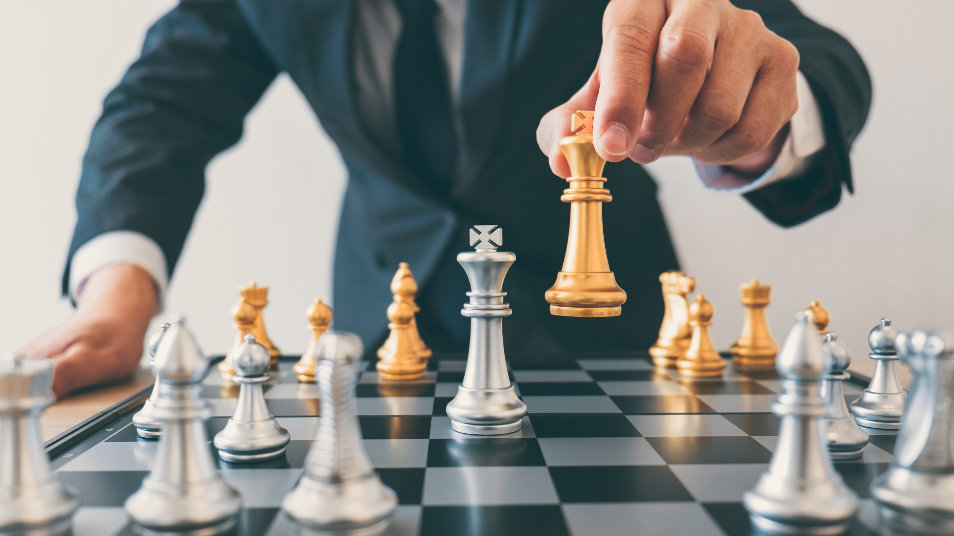Man in suit moving gold king chess piece to capture silver king.