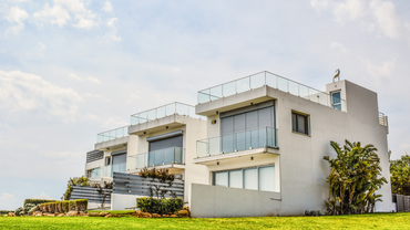 White modern beachfront homes with glass balconies under a cloudy sky.