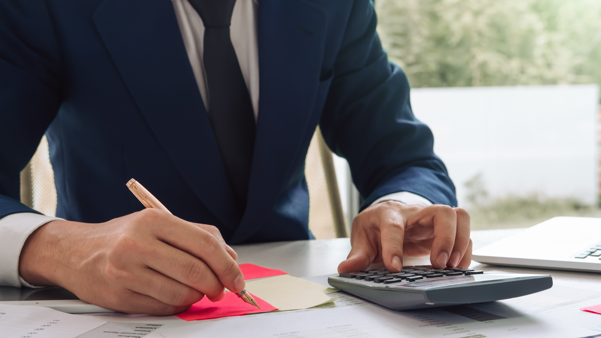 Person in blue suit calculating with calculator and writing on paper.