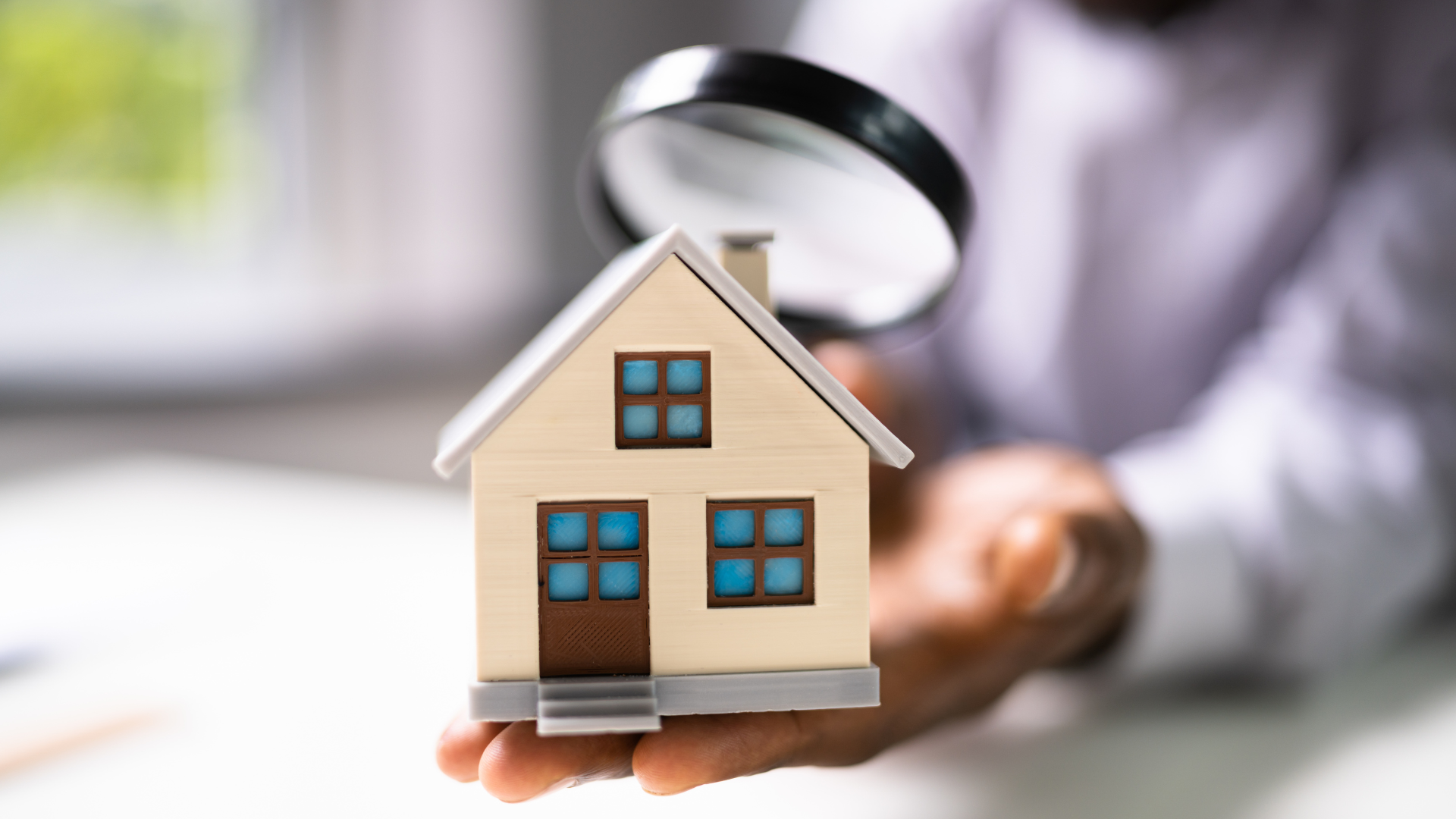Person examining a miniature house with a magnifying glass.