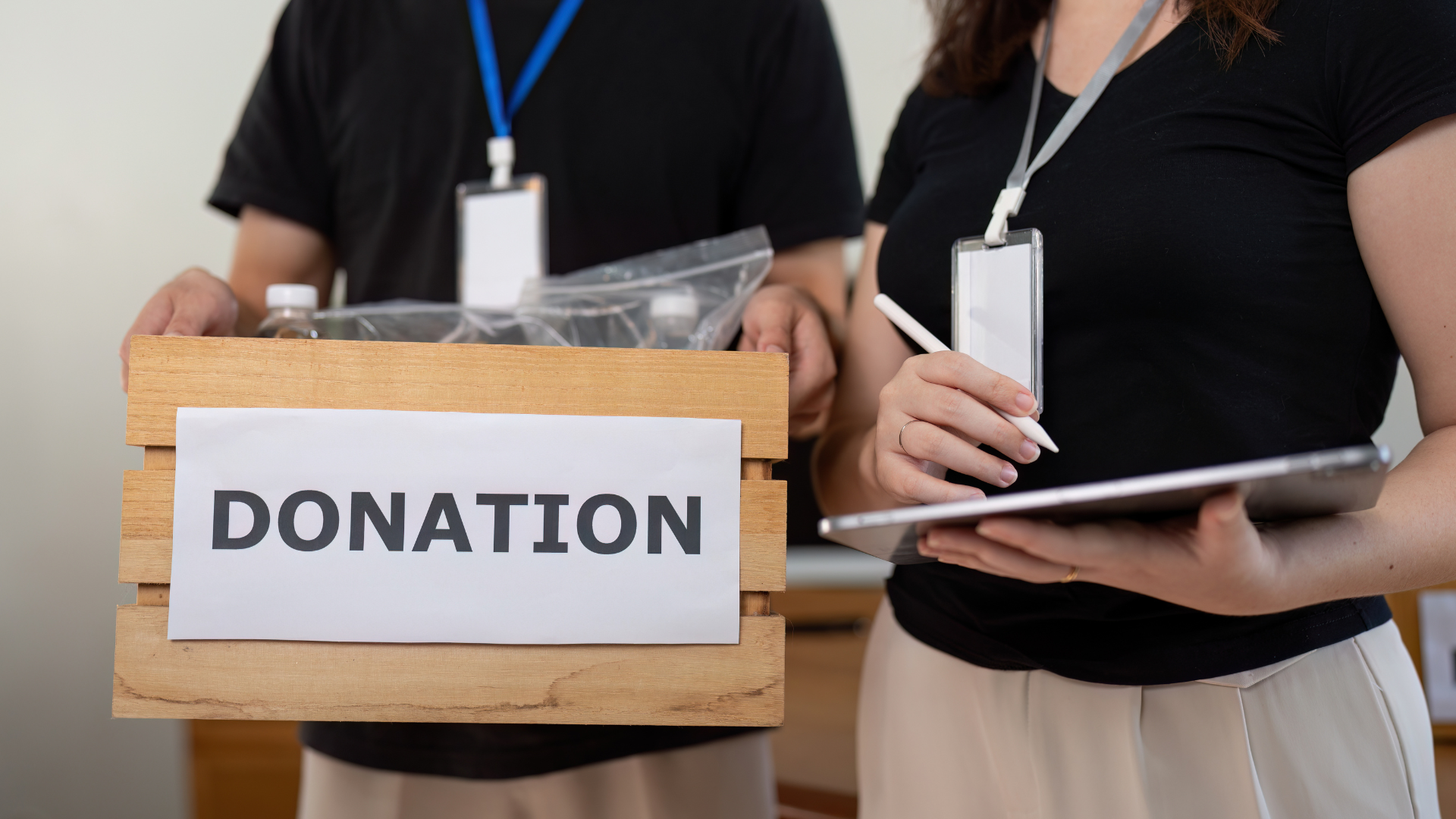 Two people holding a donation box and tablet. One holds a wooden box labeled 