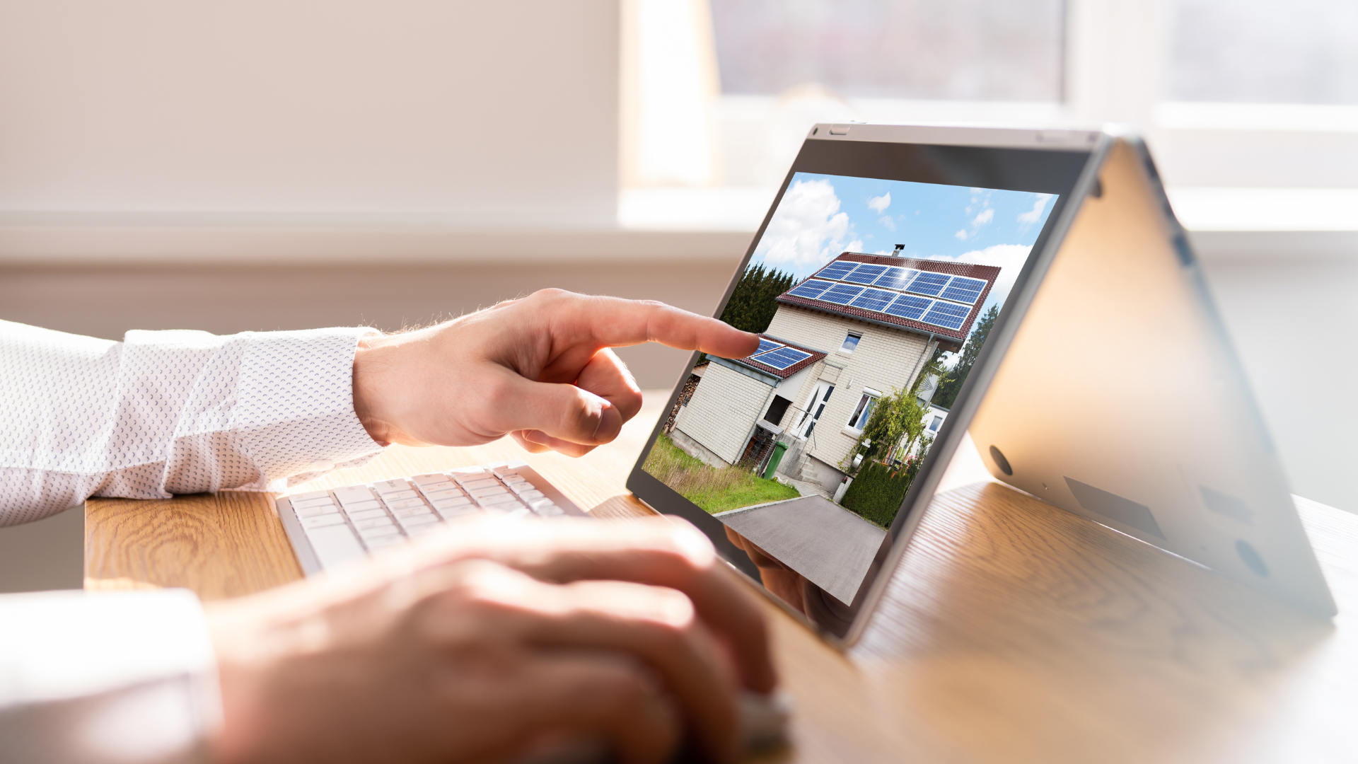 Person using a touchscreen laptop, viewing a house with solar panels on the roof.