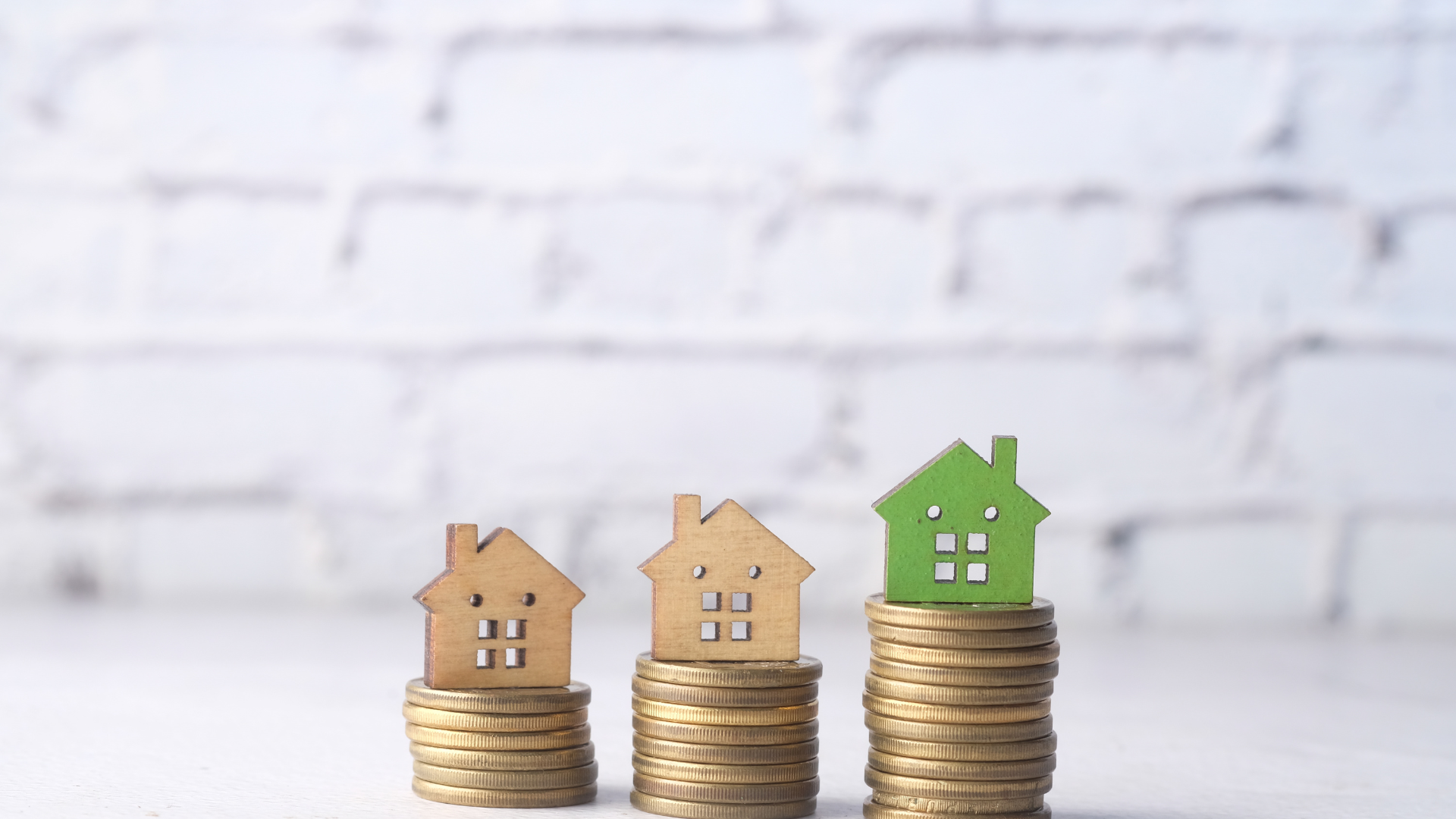 Three miniature houses on stacks of coins, increasing in height. Green house on top.