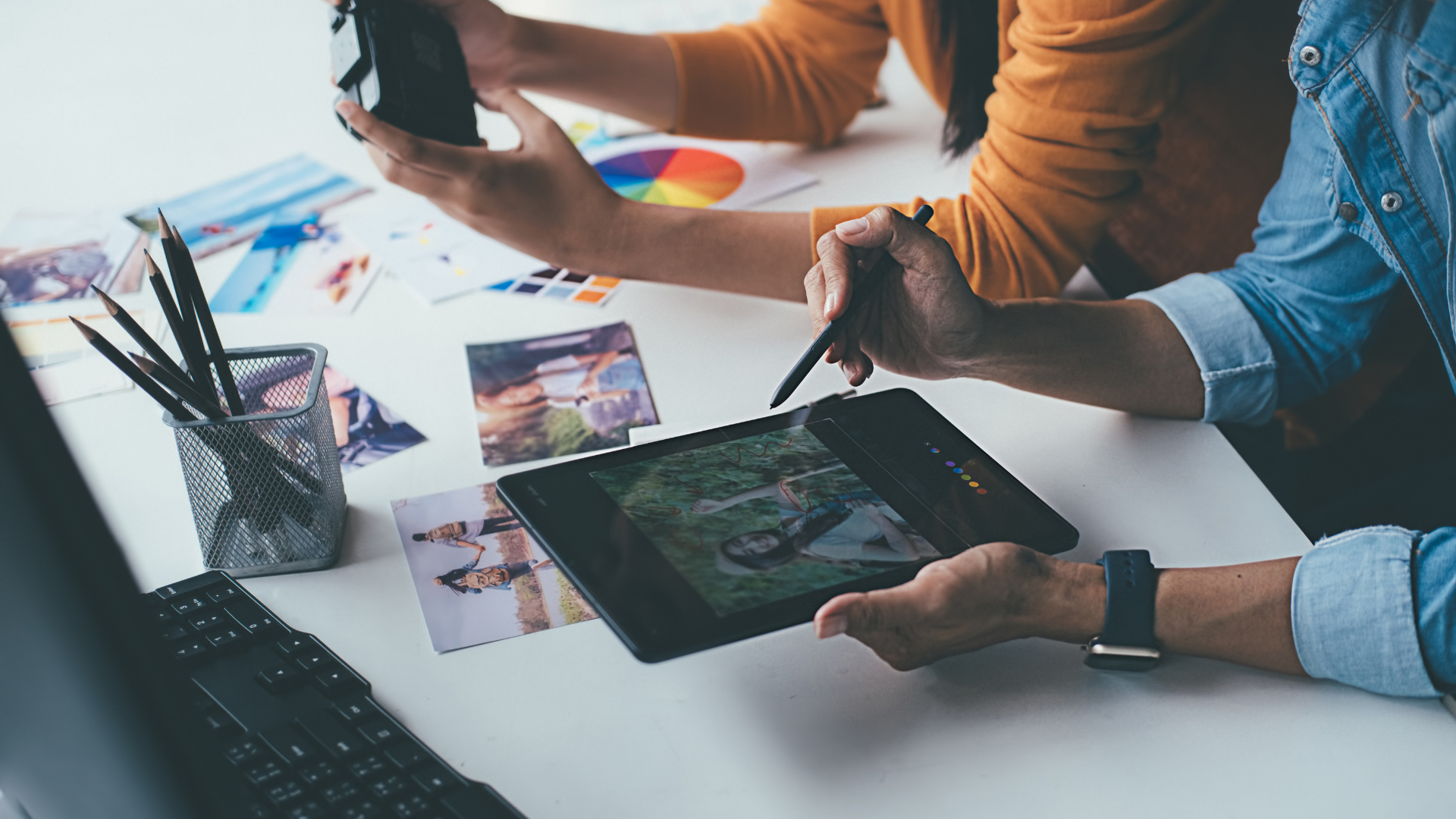People collaborating on a project, using a tablet, photos, and a color wheel at a white desk.
