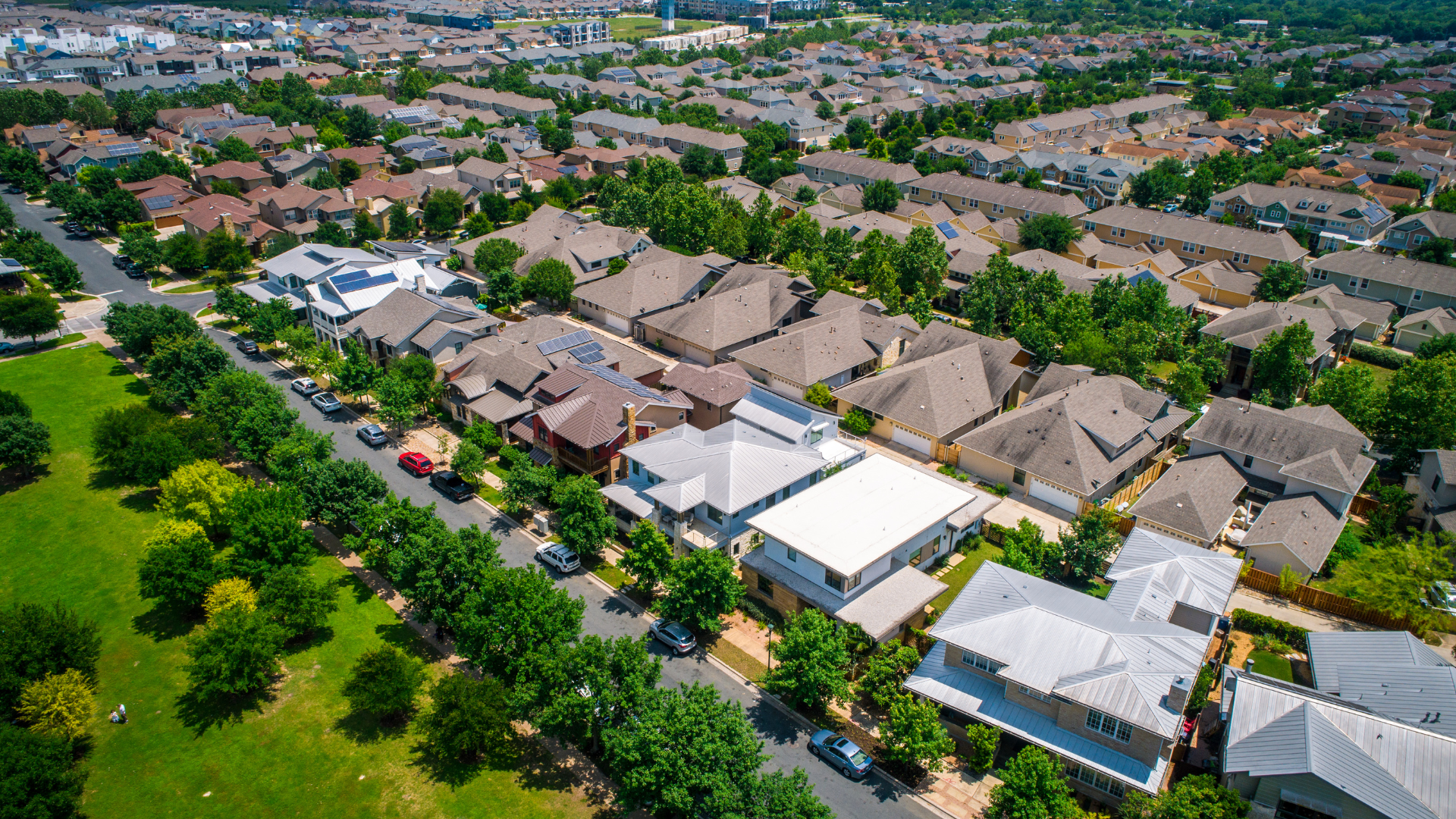 Aerial view of a residential neighborhood with houses, streets, and trees; a park is visible on the left.