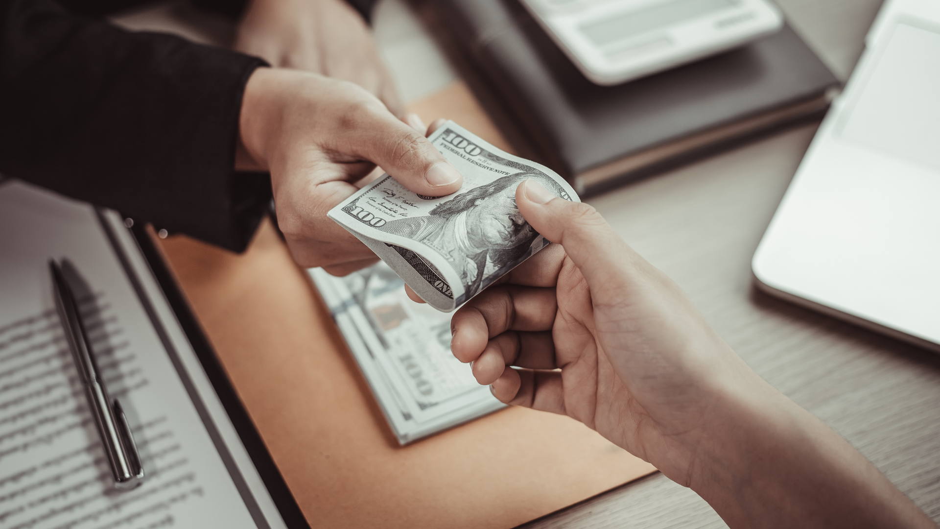 Two hands exchanging US dollar bills, possibly a transaction.