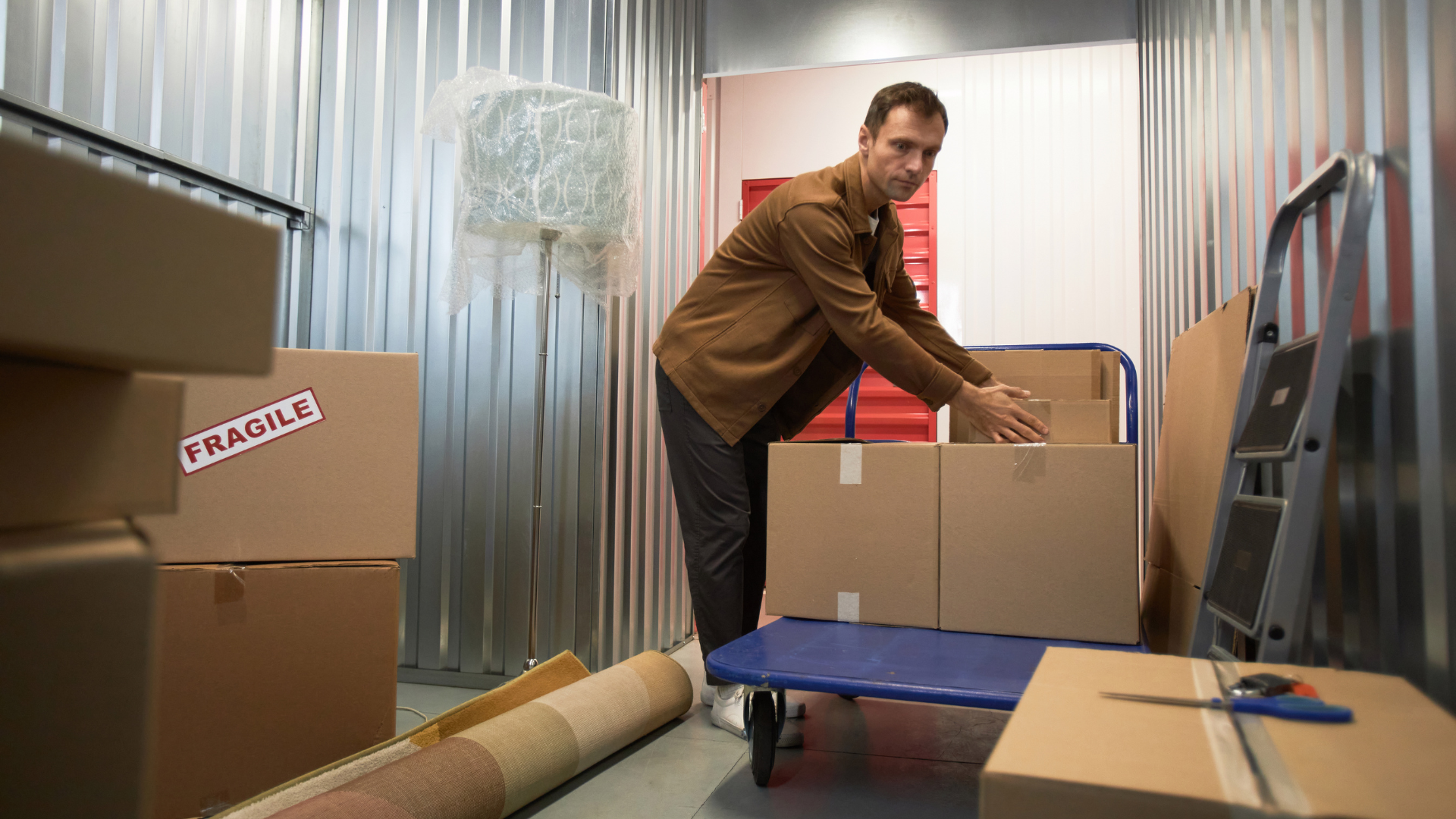 Man loading boxes into storage unit. Boxes, rug, and dolly visible.