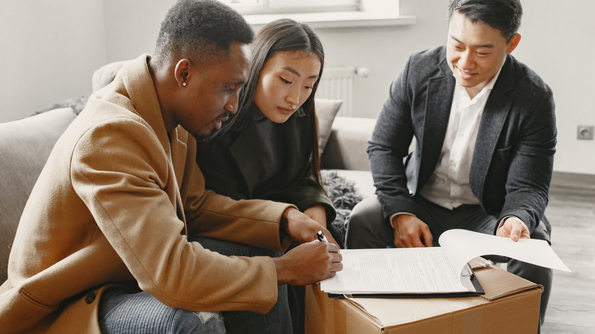 Couple signing paperwork with a realtor, in a home setting.