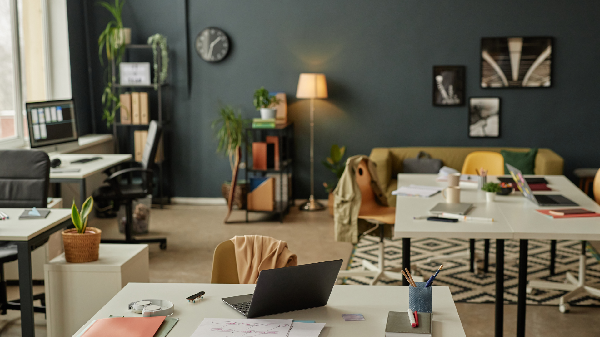 Modern office with desks, a sofa, plants, and various decor items in a room with dark teal walls.