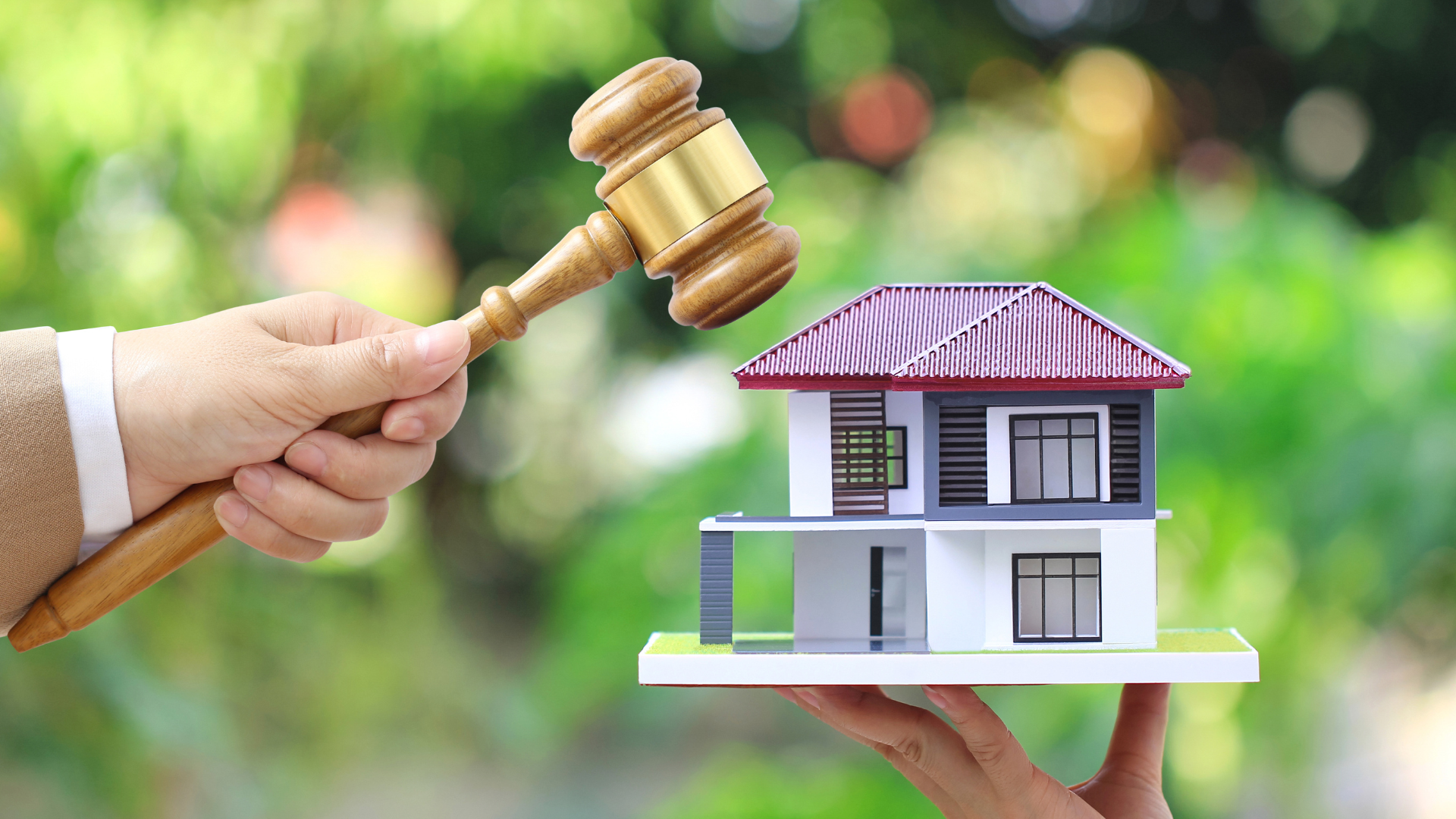 Hand holding gavel above miniature house, representing a real estate auction.