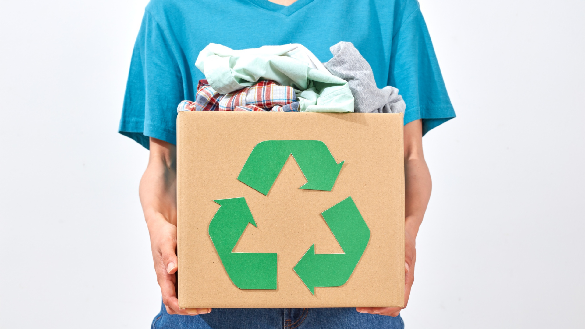 Person holding a cardboard box with a green recycling symbol and clothes.