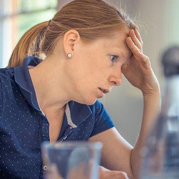 Woman with hand on forehead, looking down with a stressed expression.