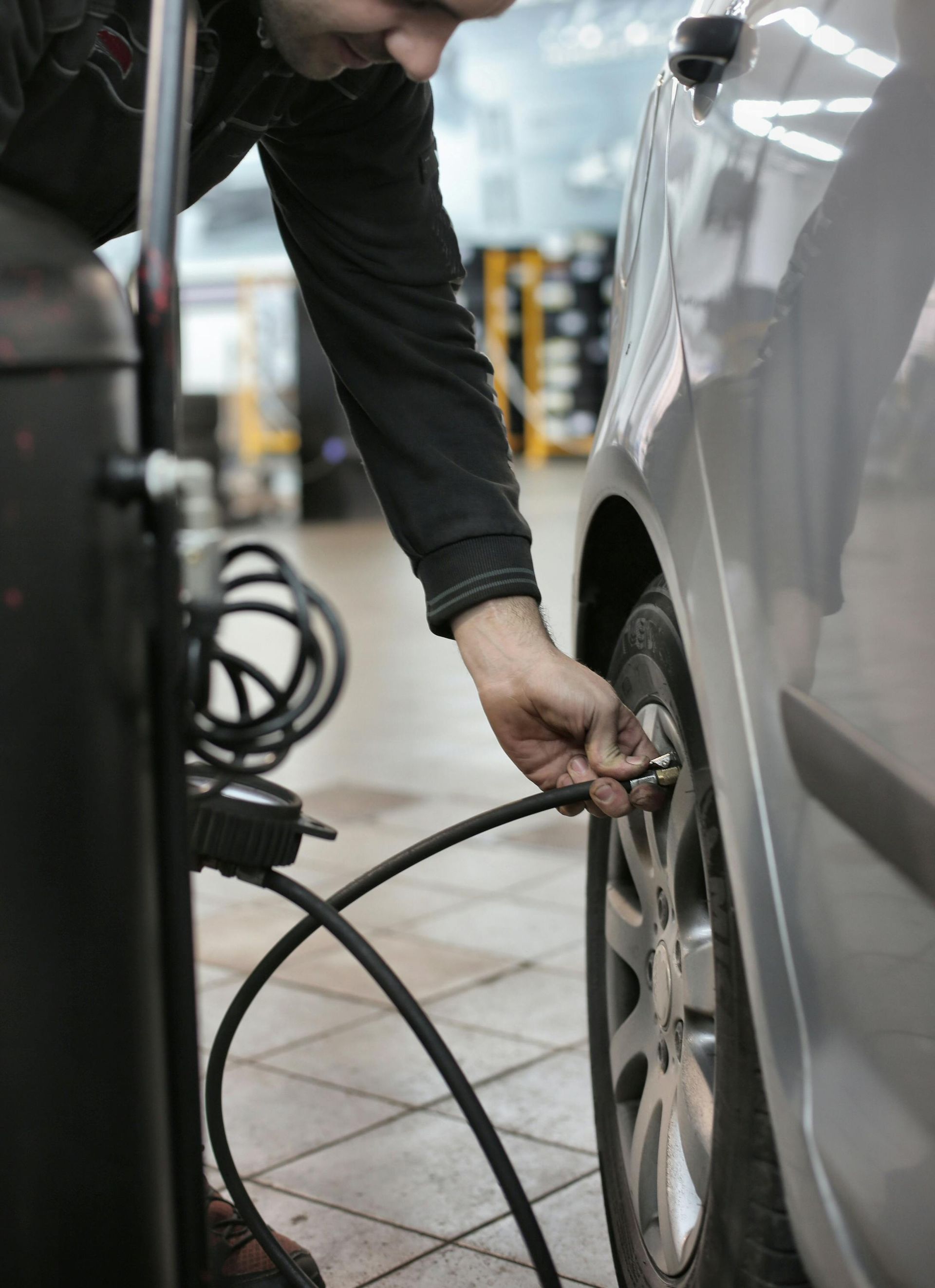 A man is pumping air into a car tire in a garage.