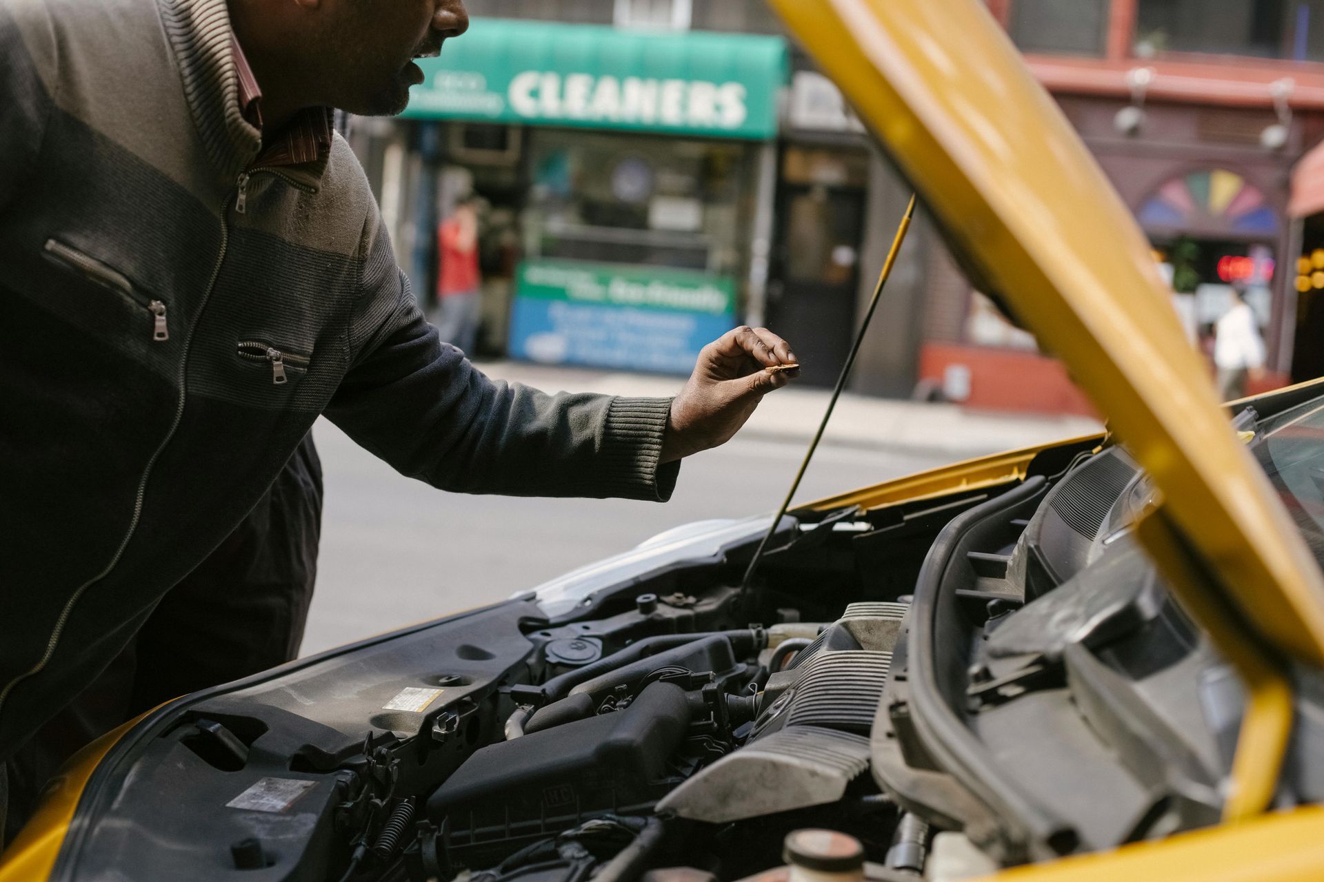 A man is looking under the hood of a yellow car.