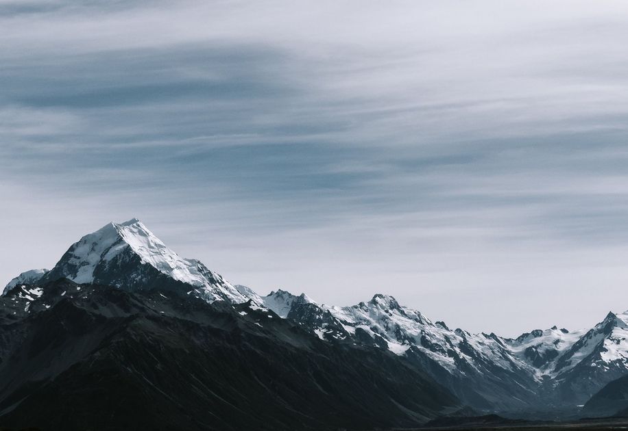 A snowy mountain range with a cloudy sky in the background