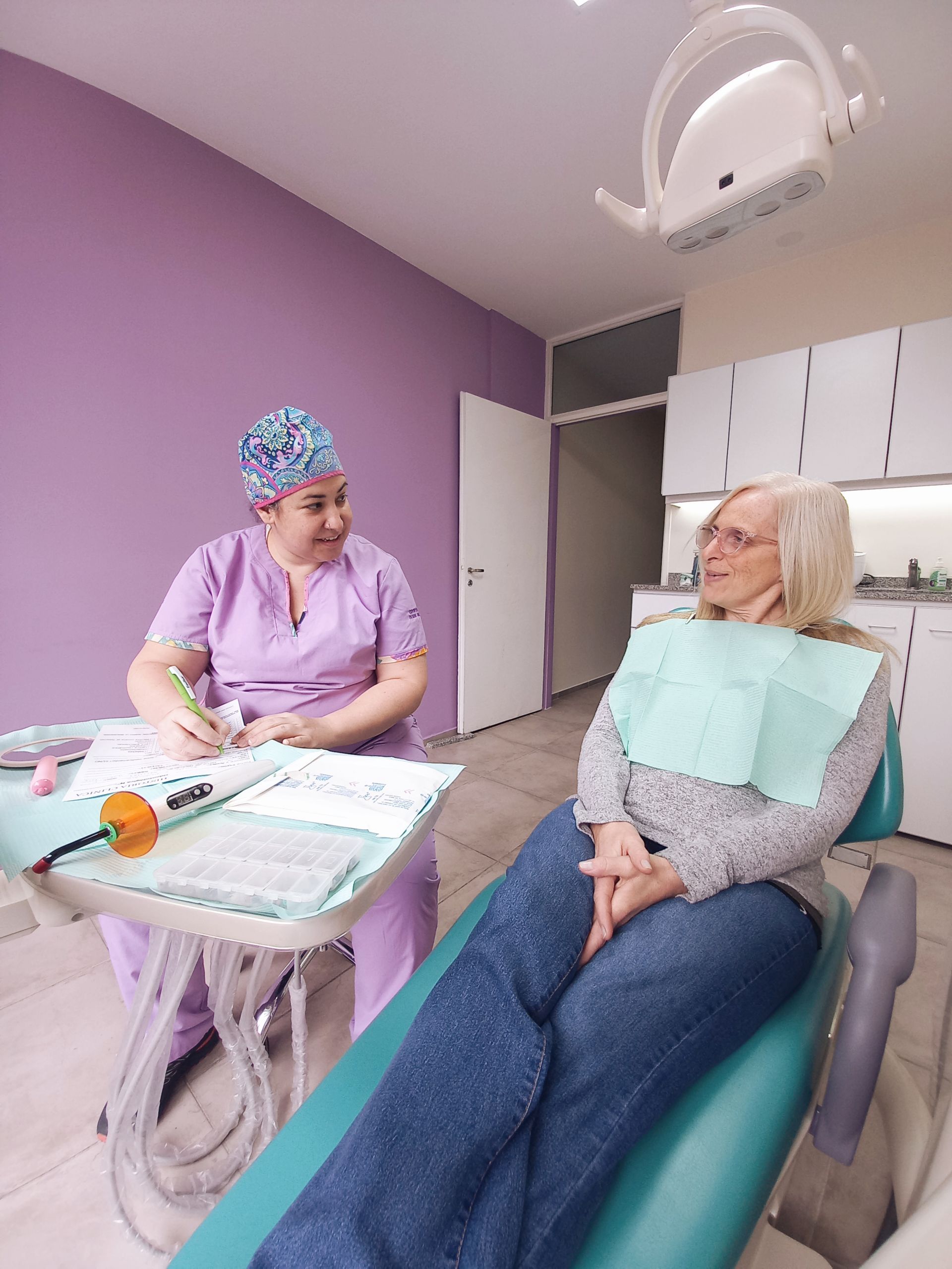 Una mujer está sentada en una silla dental hablando con un dentista.