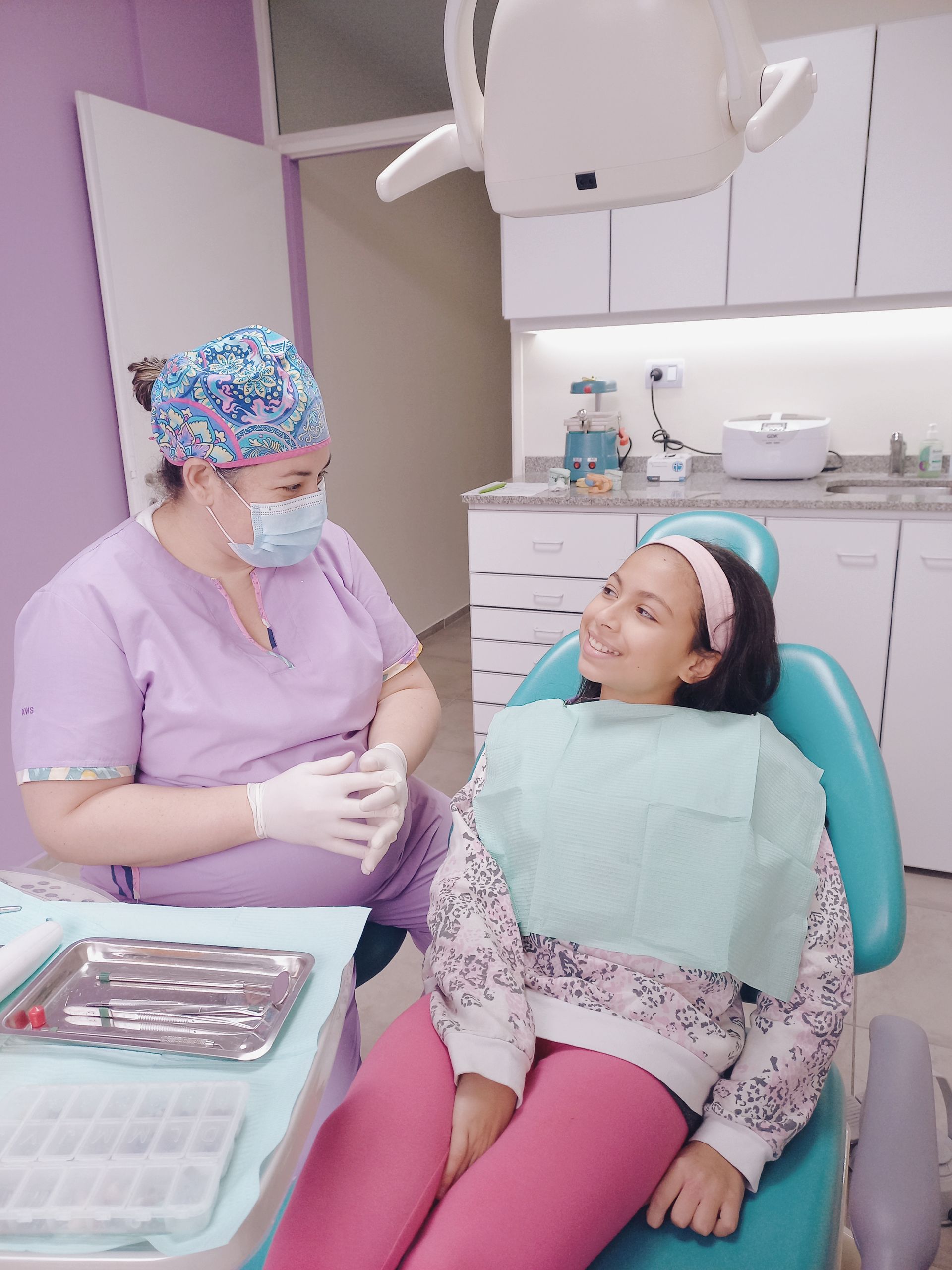 Una mujer está sentada en una silla dental hablando con un dentista.