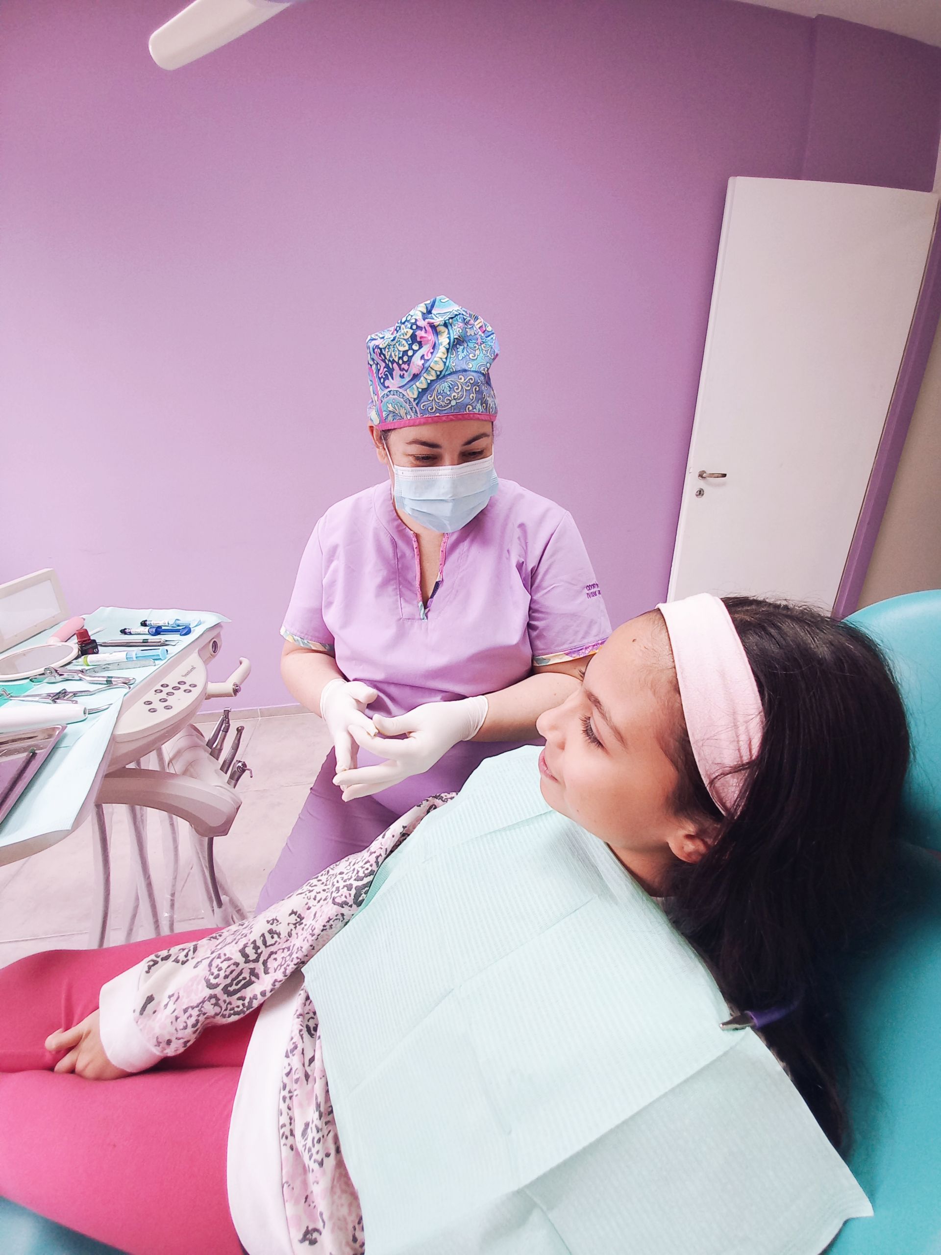Una niña está sentada en una silla dental mientras un dentista le examina los dientes.