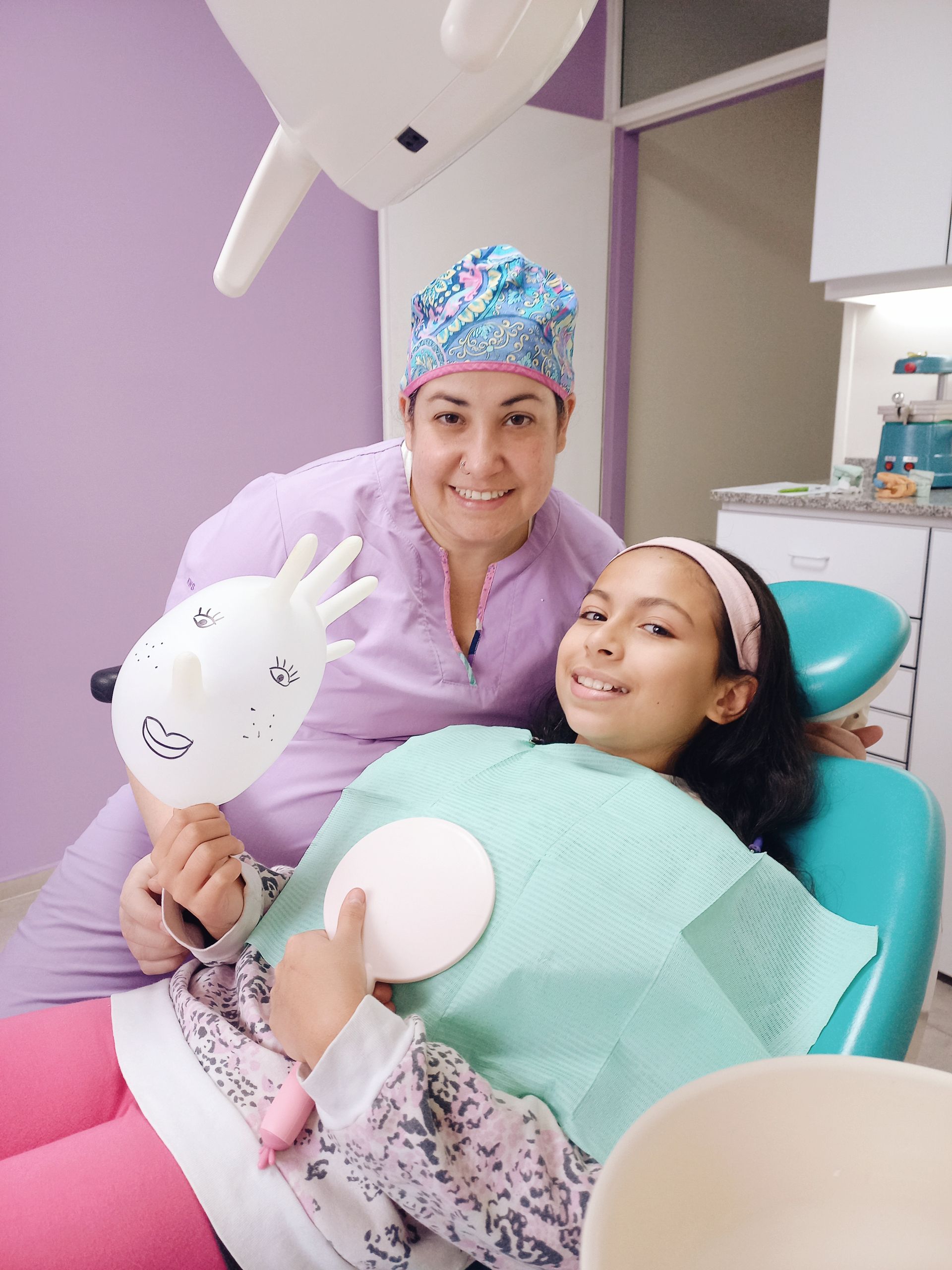 Una mujer sostiene un globo frente a una niña en una silla dental.