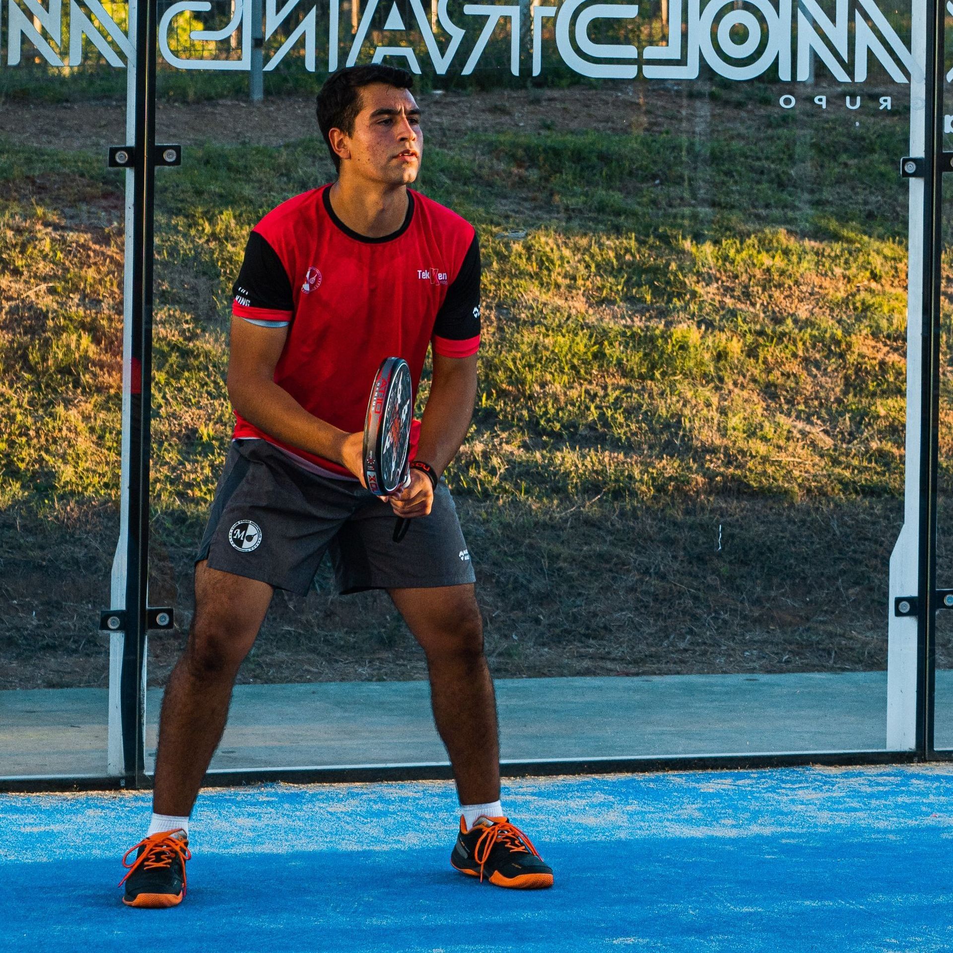 Een man in een rood shirt houdt een tennisracket vast