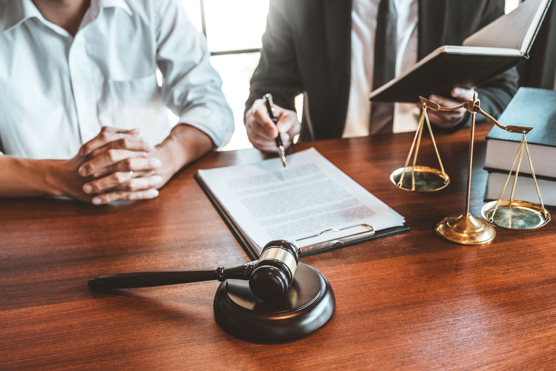 Lawyer and client review documents at a wooden table with a gavel, scales, and books.