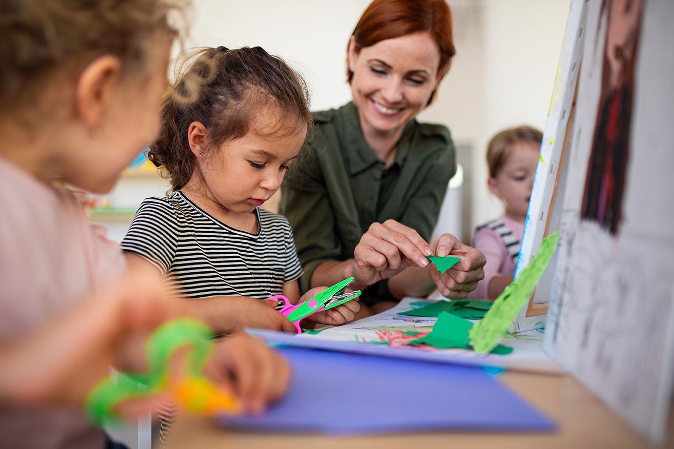 Teacher and children in a classroom, creating art with green shapes.