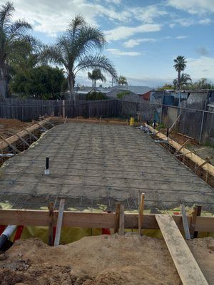 Construction site with concrete foundation and rebar mesh, wooden frame, and plumbing.