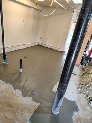 A room under construction with a wet cement floor, black pipes, and beige walls.
