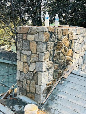 Stone chimney under construction on a rooftop with two water bottles on top.
