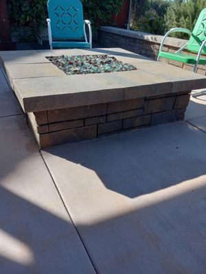 Stone fire pit with blue glass on a patio with two chairs.