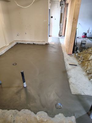 Concrete floor poured in a room with plumbing fixtures and doorway. Construction site.