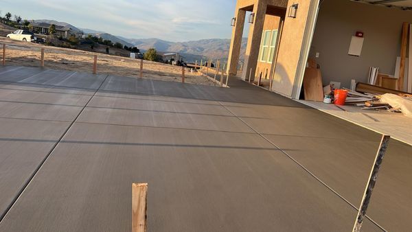 Newly poured concrete driveway with wooden stakes, leading to a house with a garage and mountain view.