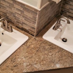 Two white sinks with silver faucets on a speckled countertop, against a tiled backsplash.