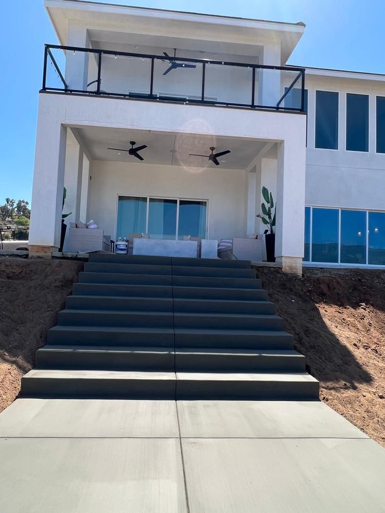 Concrete steps leading up to a white house with a balcony, patio, and large windows.