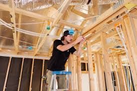 A man is standing on a ladder working on the ceiling of a house under construction.