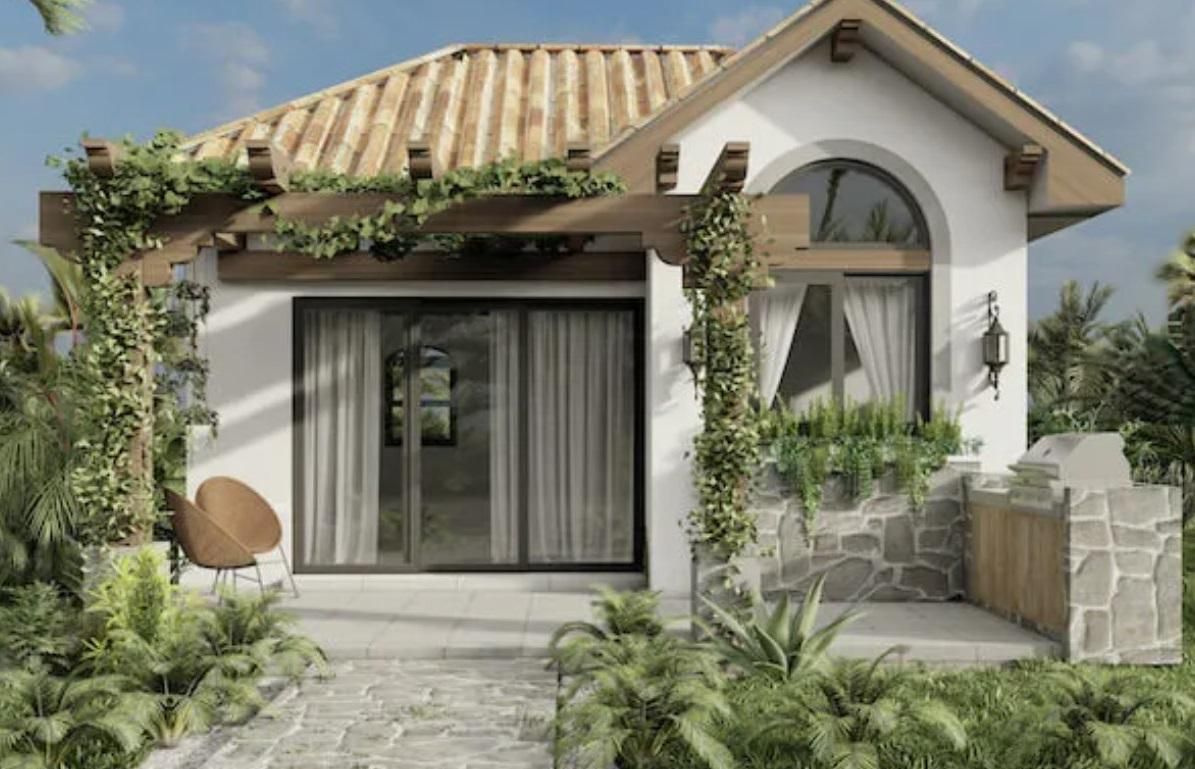 A small white ADU with a tiled roof is surrounded by lush greenery.